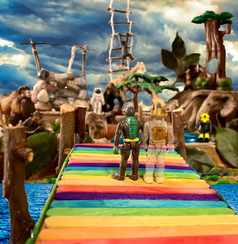 2 toys hand in hand on a rainbow dock, 1 toy is faded. In the back are 2 other toys, a wishing well, trees, and animals